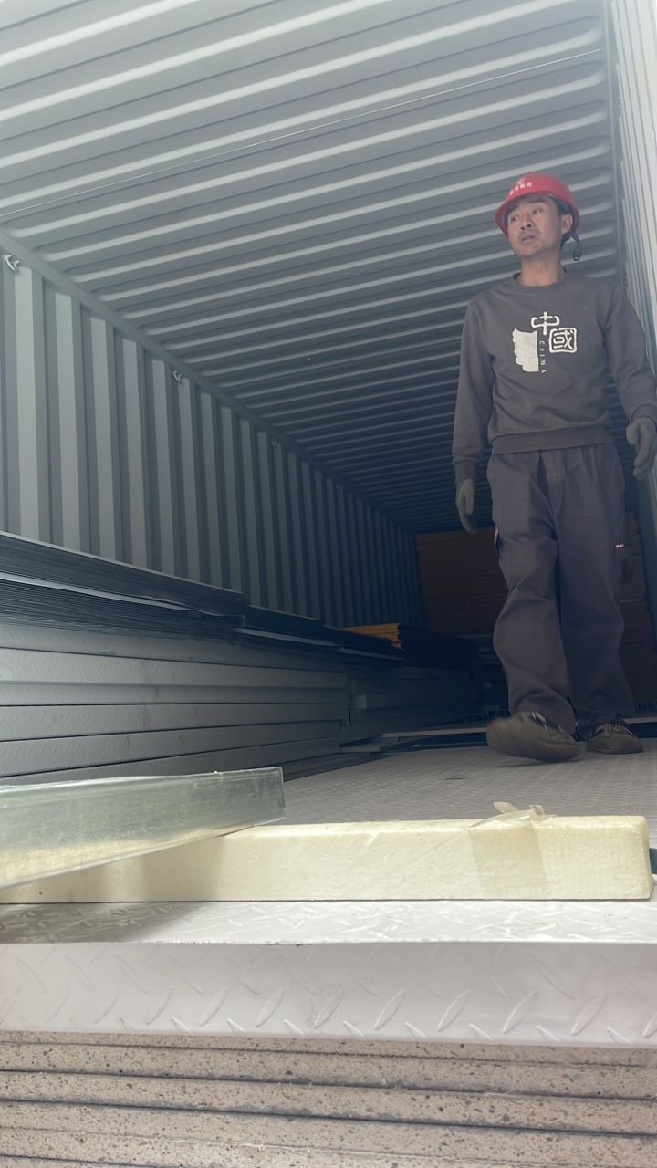 Inside the loaded container showing stacked SIP panels and a worker in safety gear
