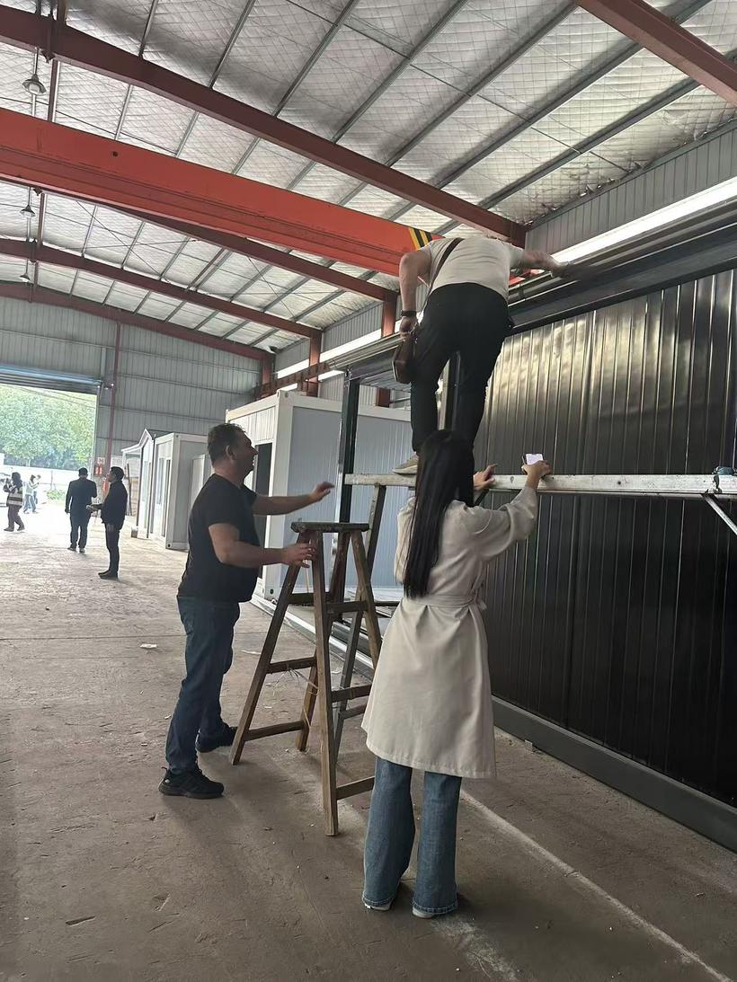 Client on ladder examining upper wall and roof interface of modular building while Taimao team provides guidance