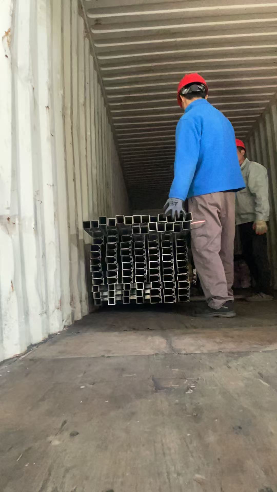 Worker carrying a bundle of square steel tubes into the container