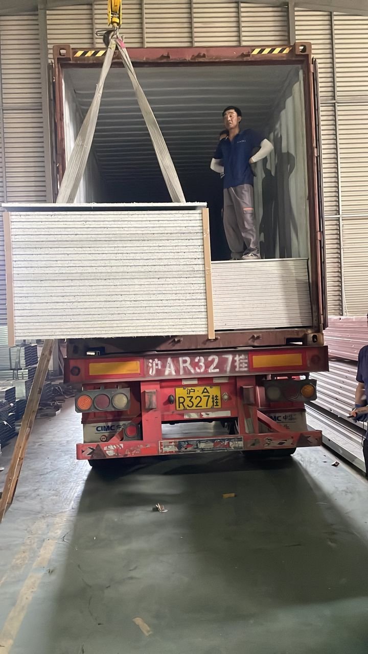 Crane lifting large SIP panel into container truck at factory