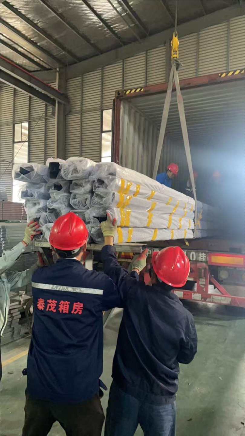Workers loading bundled SIP panels into container using crane